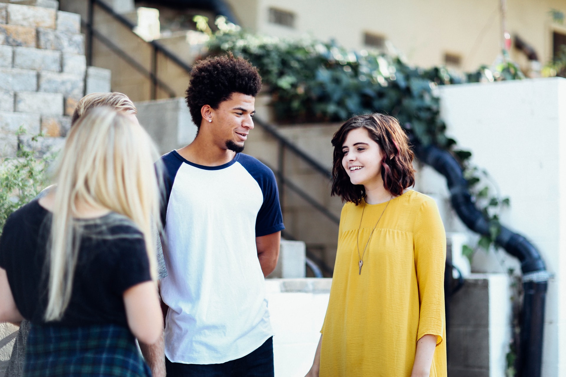 I group of teens stand together in conversation in front of a staircase