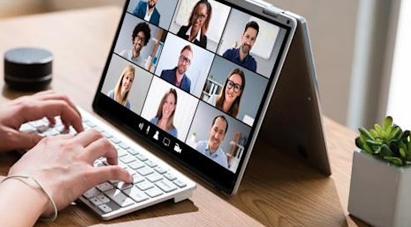 hands type on a keyboard in front of an open tablet hosting a virtual meeting.