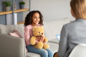 Child chats with psychologist while holding teddy bear